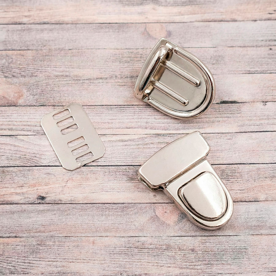 Juego completo de cierre metálico para bolso color plata (3x4 cm) con anverso, reverso y placa de fijación sobre fondo de madera.