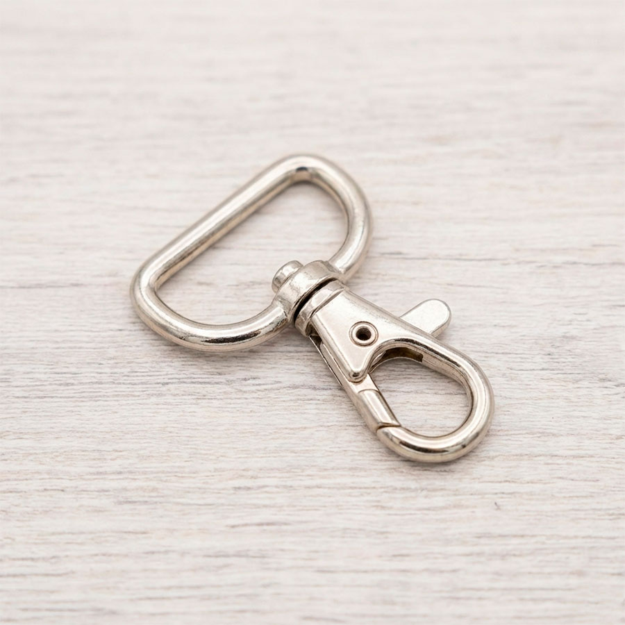 Mosquetón metálico de color plata de 2,5 cm de ancho para correas de bolsos y mochilas sobre fondo de madera clara.