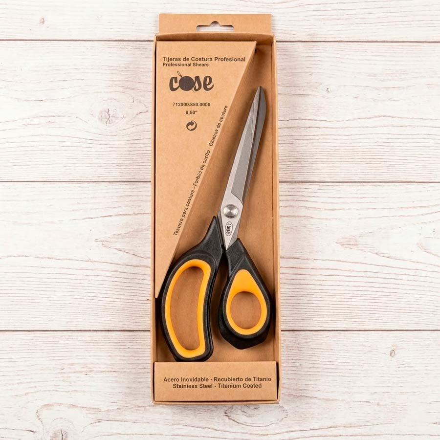 Tijeras de costura profesional marca Cose de 8,50 pulgadas, con hojas recubiertas de titanio y mango ergonómico negro y amarillo en su caja de cartón.